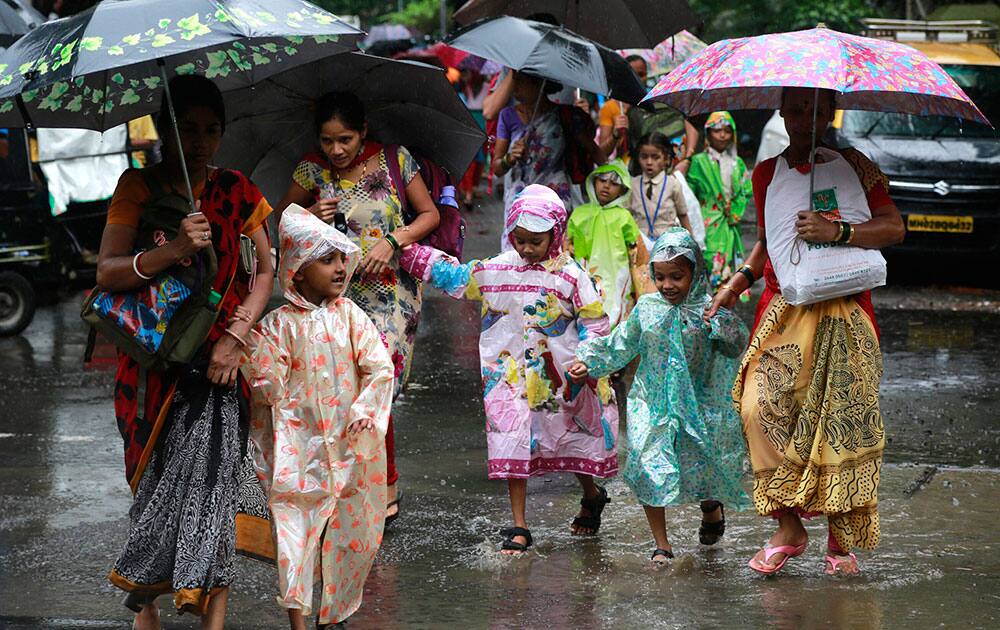 Mothers walk with their children wearing raincoats as they cross a flooded road in Mumbai. Mothers walk with their children wearing raincoats as they cross a flooded road in Mumbai.