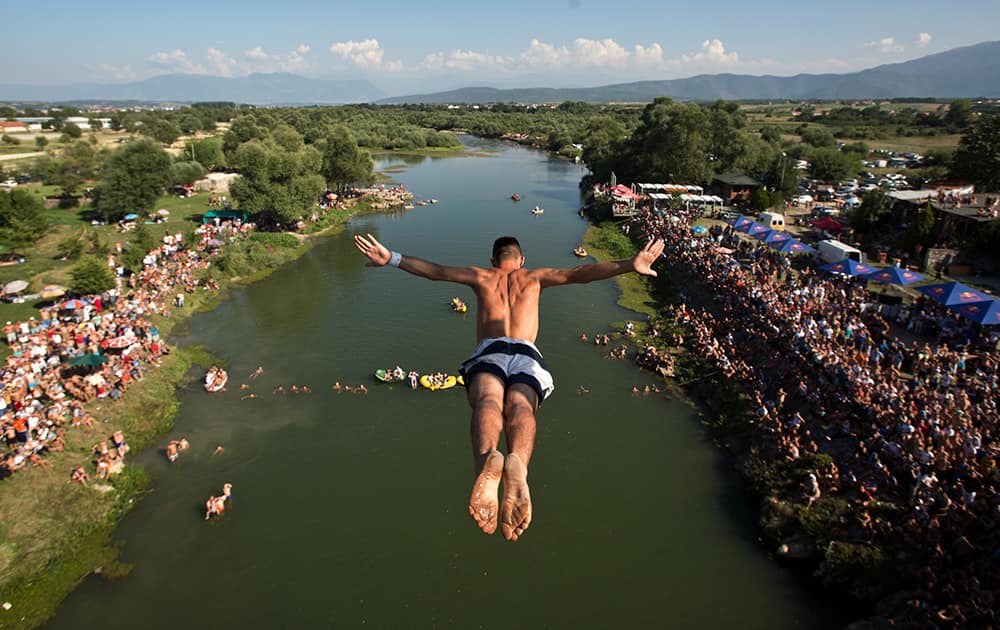 Spectators watch from the river banks as a diver launches from the Ura e Shenjte bridge