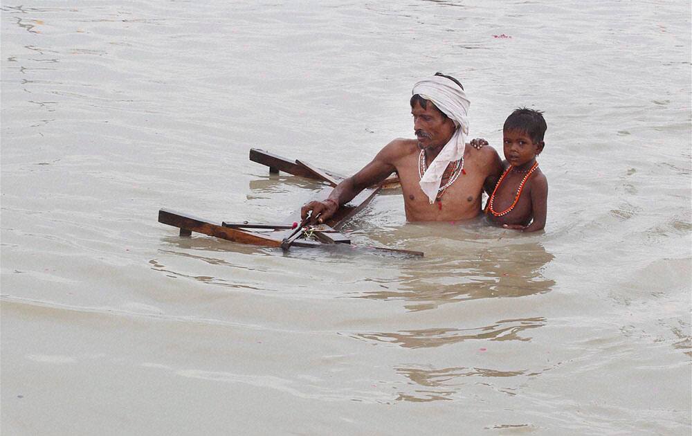 A hindu priest carries his son and puls wooden bed in flooded water of river Ganga after heavy monsoon rain in Allahabad A hindu priest carries his son and puls wooden bed in flooded water of river Ganga after heavy monsoon rain in Allahabad