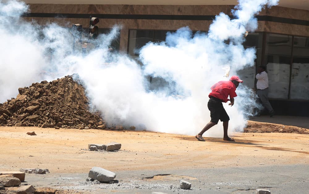 A protestor throws back a teargas canister at police in Harare