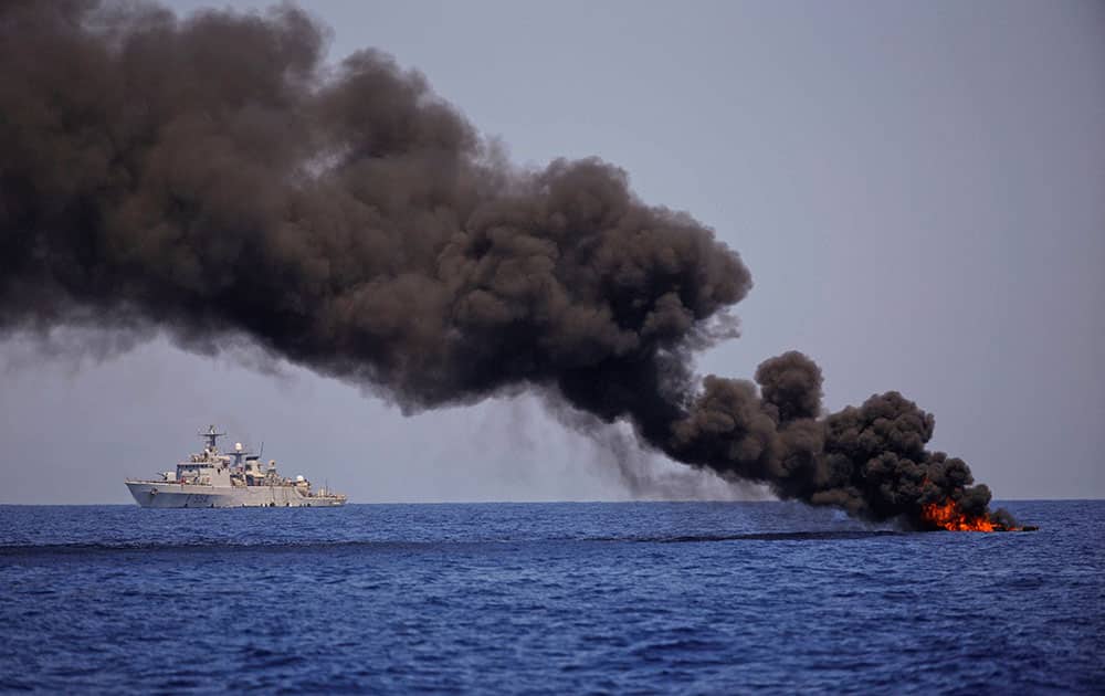 An Italian Navy ship sails past a burning dinghy after evacuating the migrants sailing on it in the Mediterranean sea toward the Italian coasts