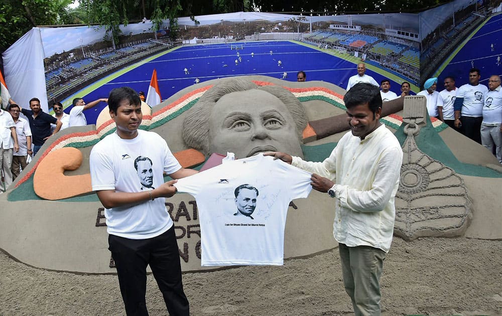 Former hockey player and MP Dilip Tirkey and sand artist Sudarshan Patnaik unveil a jersey in front of a sand image created by the latter at a demonstration to demand Bharat Ratna honour for hockey legend Dhyan Chand