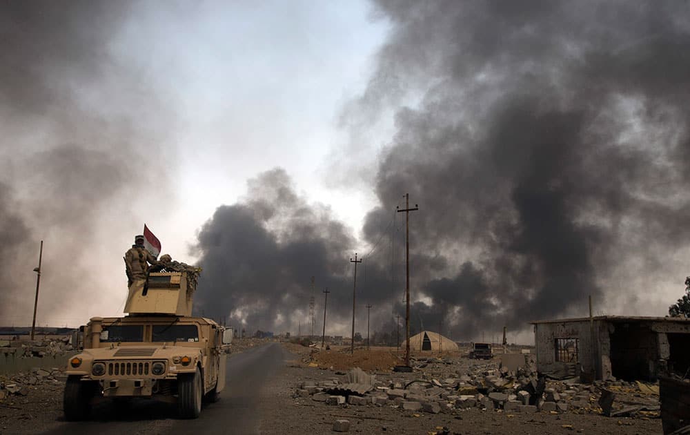 Iraqi security forces patrol as smoke rises from burning oil wells in Qayara