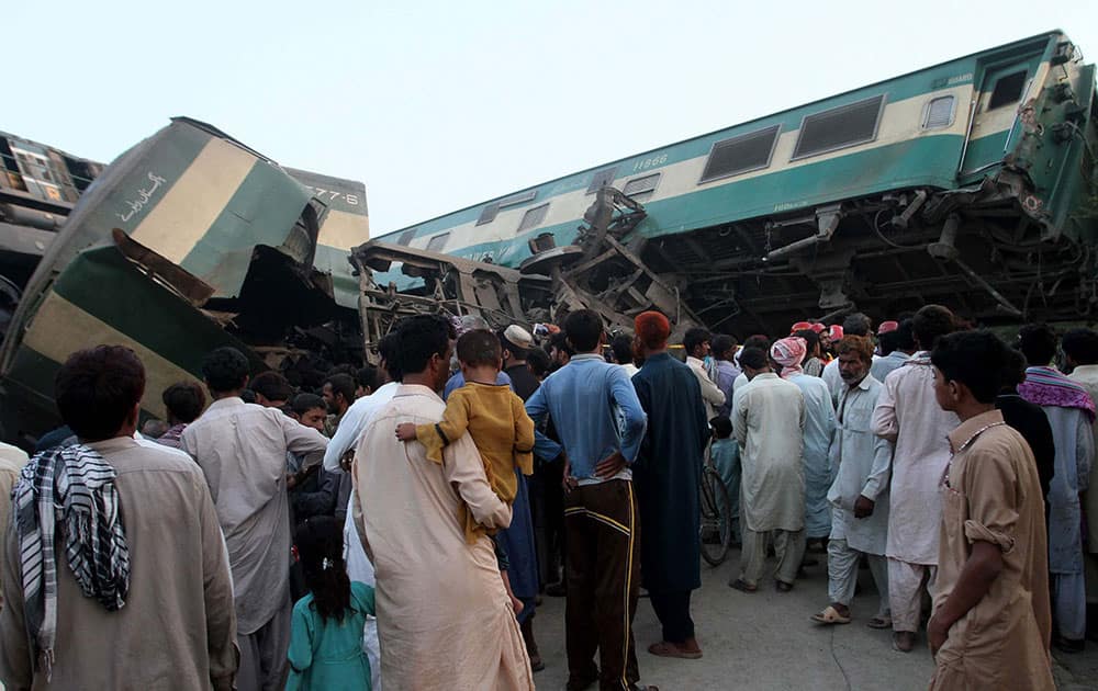 People look at a mangled passenger train that had collided with freight train near Multan, Pakistan