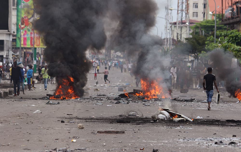 People walk near burning debris during election protests in Kinshasa