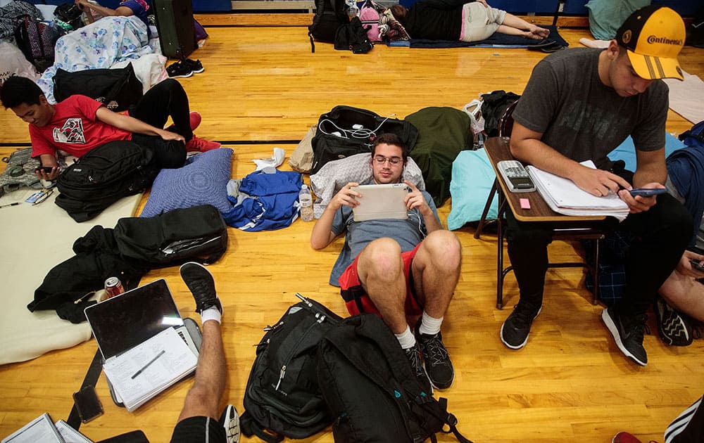 (L to R) Embry-Riddle Aeronautical University student TJ Rusiniak watches weather updates on his iPad at a public shelter set up at Mainland High School