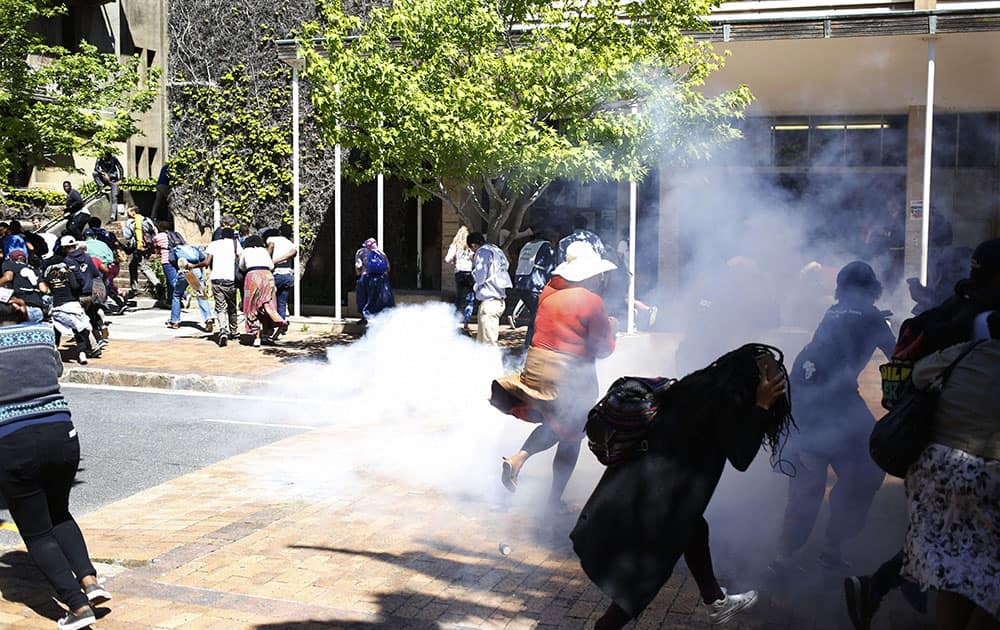 Students run away from a stun grenade that South African police used to disperse the students after they broke windows at the University of Cape town campus