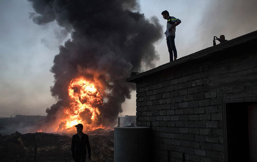 People watch as safety workers try to extinguish fire from a burning oil field in Qayara,