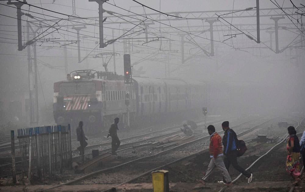 People cross railway tracks on a foggy day in Patna