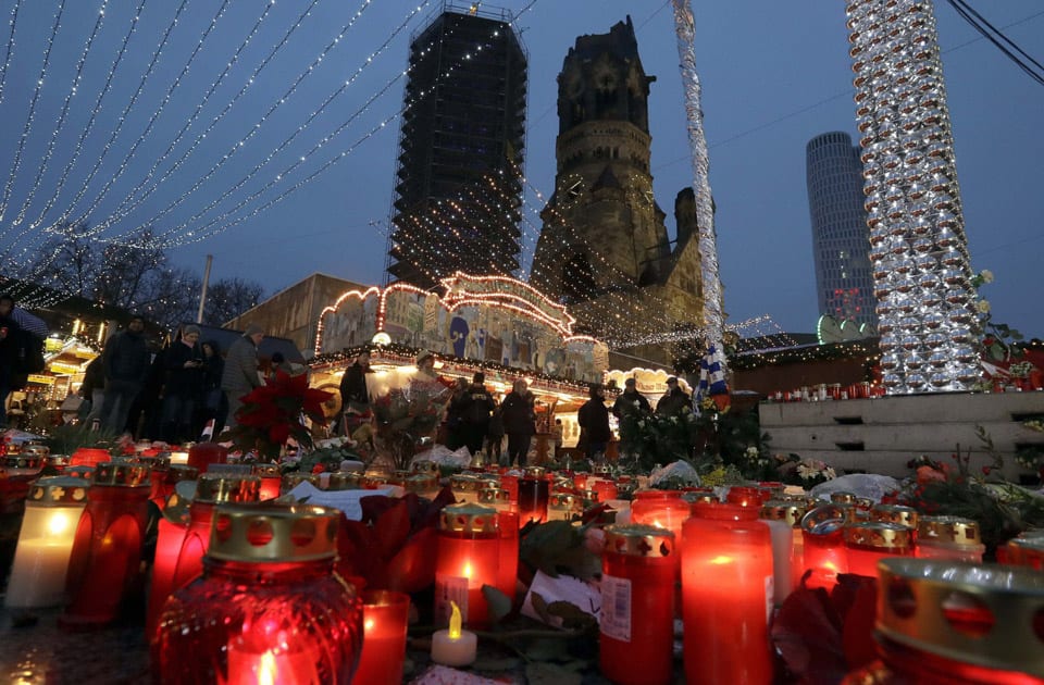 People walk past candles and flowers