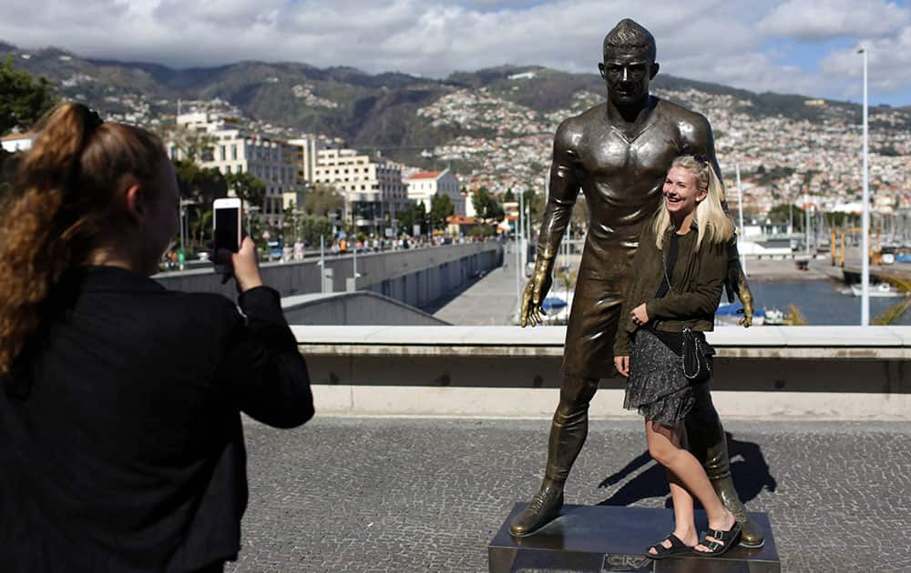 A tourist poses for a picture by a statue of Cristiano Ronaldo