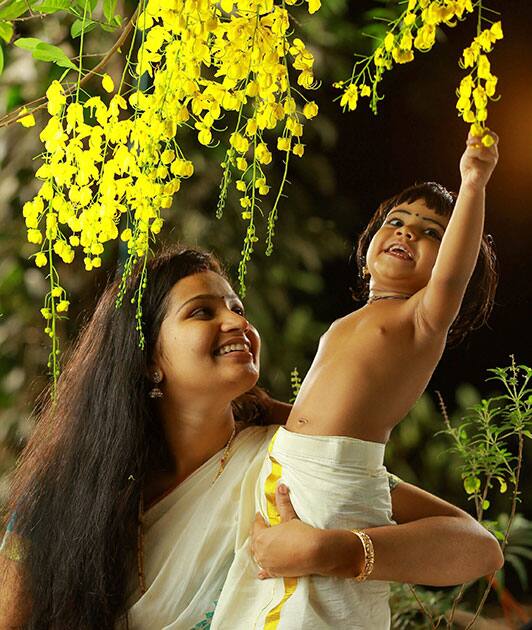 A mother holds her child who tries to pick some flowers off a Kanikkonna tree