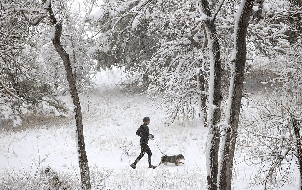 A woman and her dog run in snow following an overnight storm in Boulder