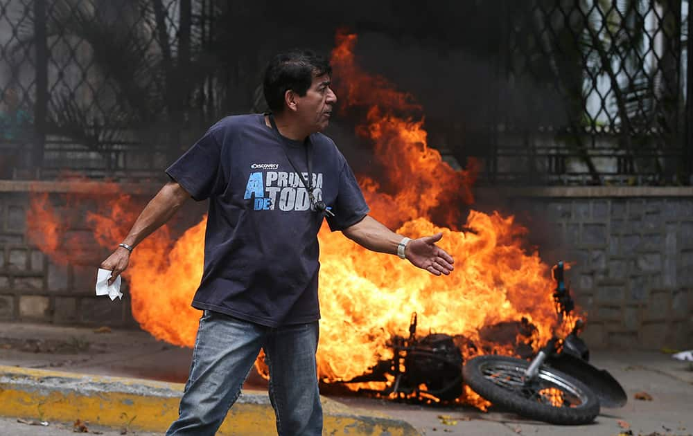 A man walks past a burning motorbike