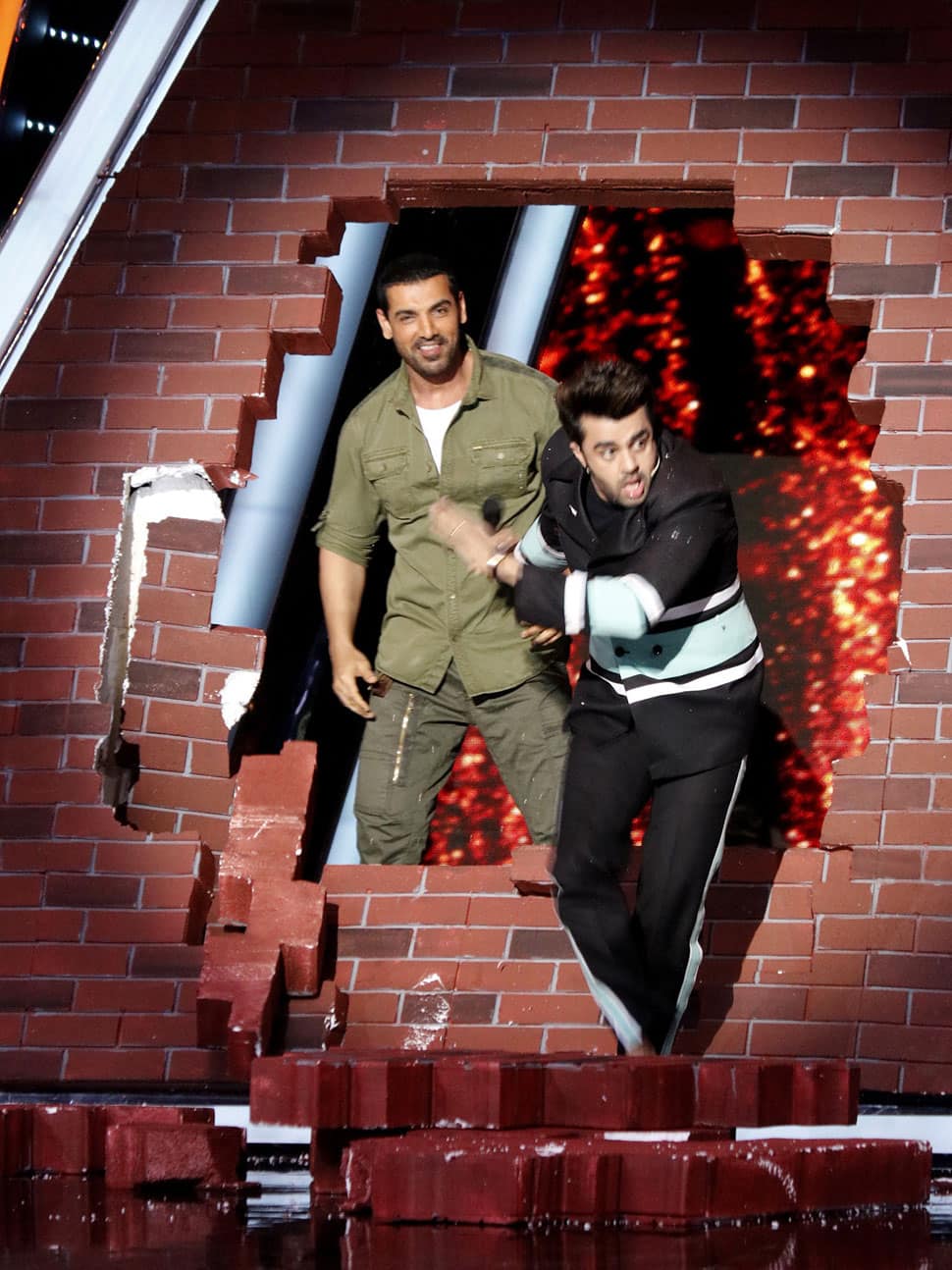 John Abraham breaks a wall made of fake bricks.
