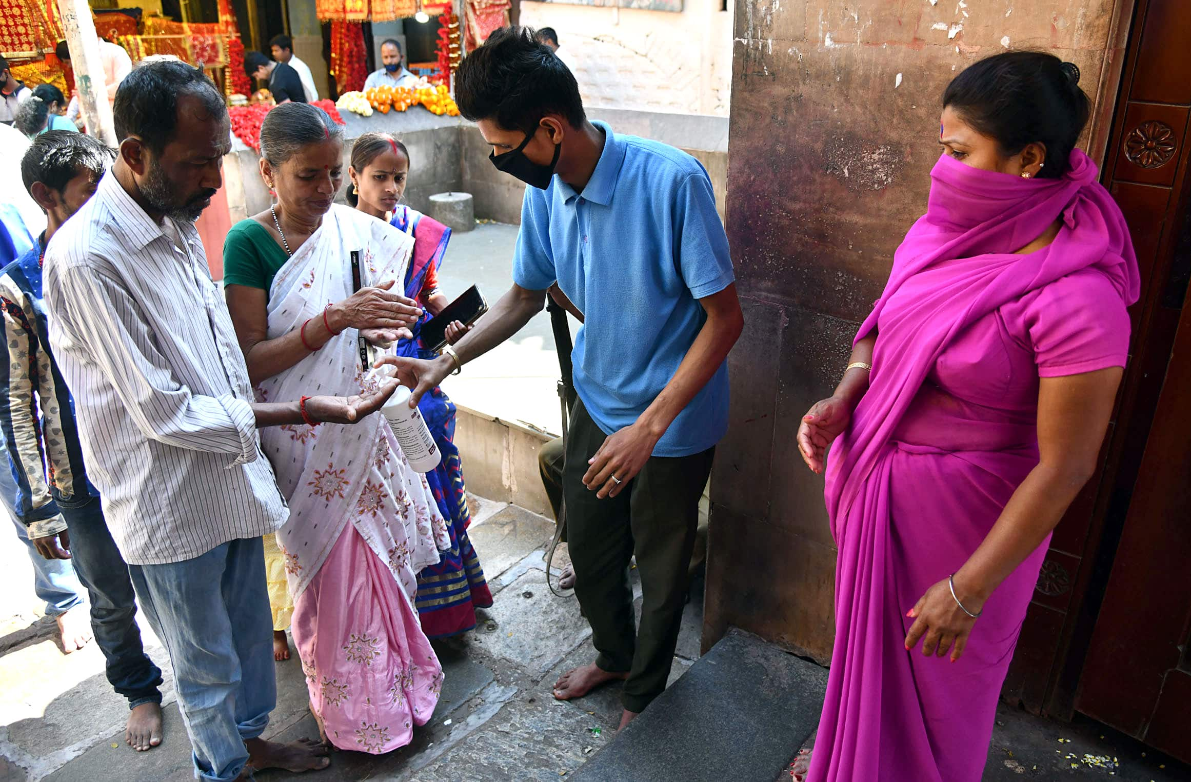 Man applies sanitizer to devotees as they arrive to offer prayers