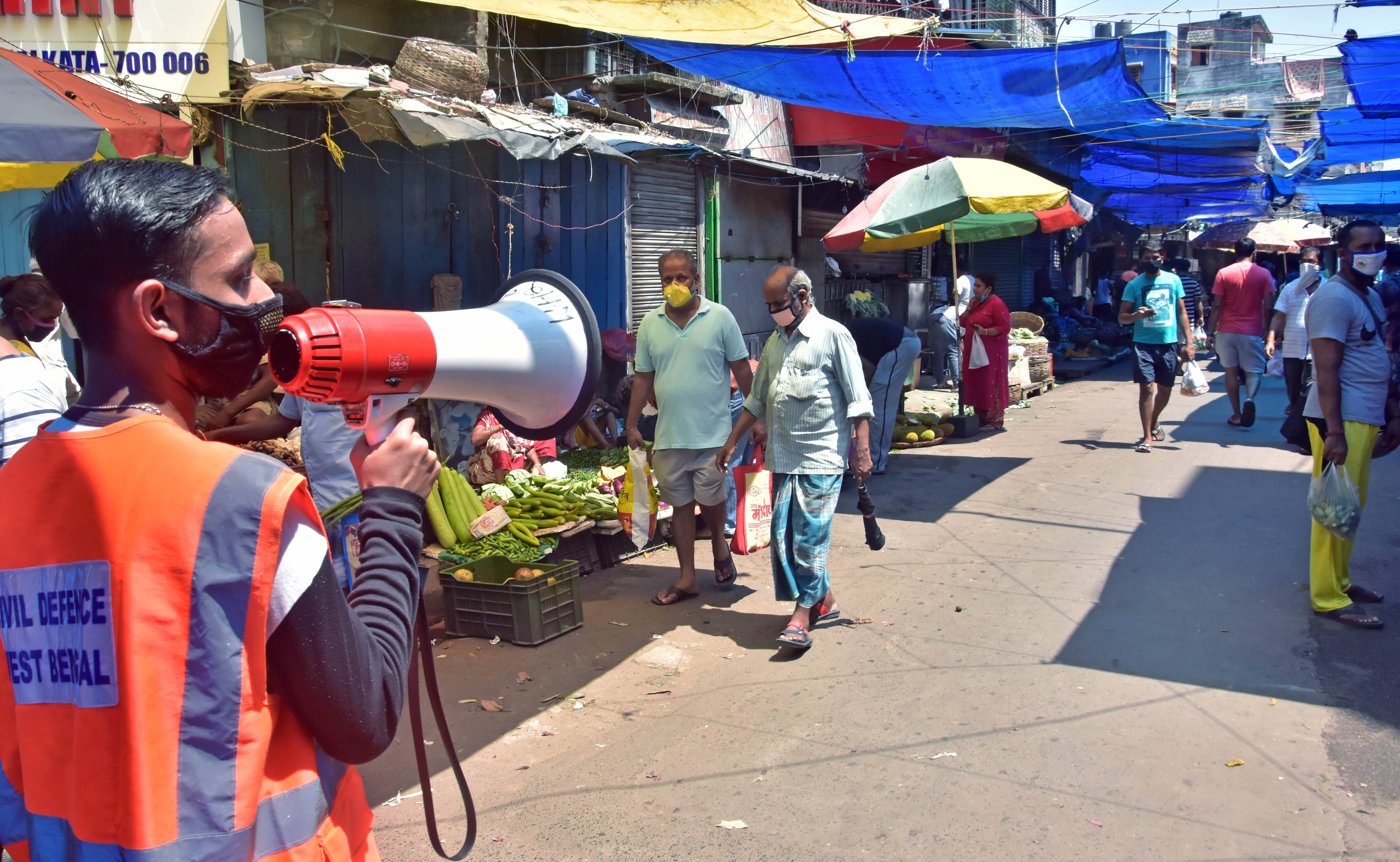 Civil Defence Staff personnel instructs people to maintain social distancing at a Kolkata market