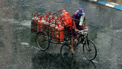 A worker carries LPG cylinders on a tricycle during rains ahead of Cyclone Yaas