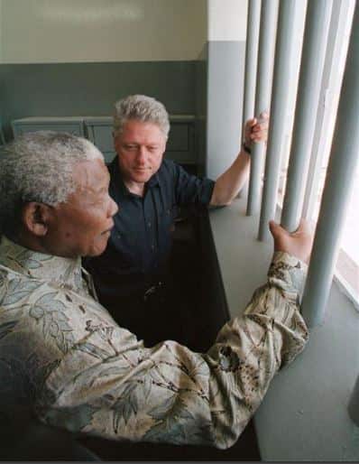 Then President Bill Clinton looks toward Nelson Mandela