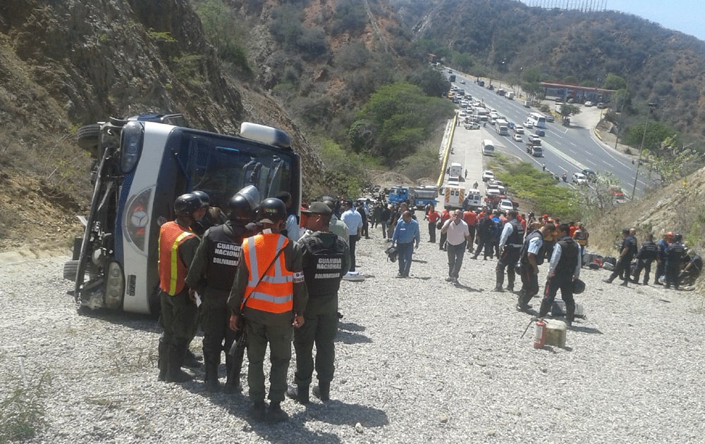 Emergency personnel and members of Agentina's Huracan soccer team, in red shirts and black shorts, mill around the wreck of the bus that was transporting the team to the airport, after it lost its brakes, lost control and flipped over, in Caracas.