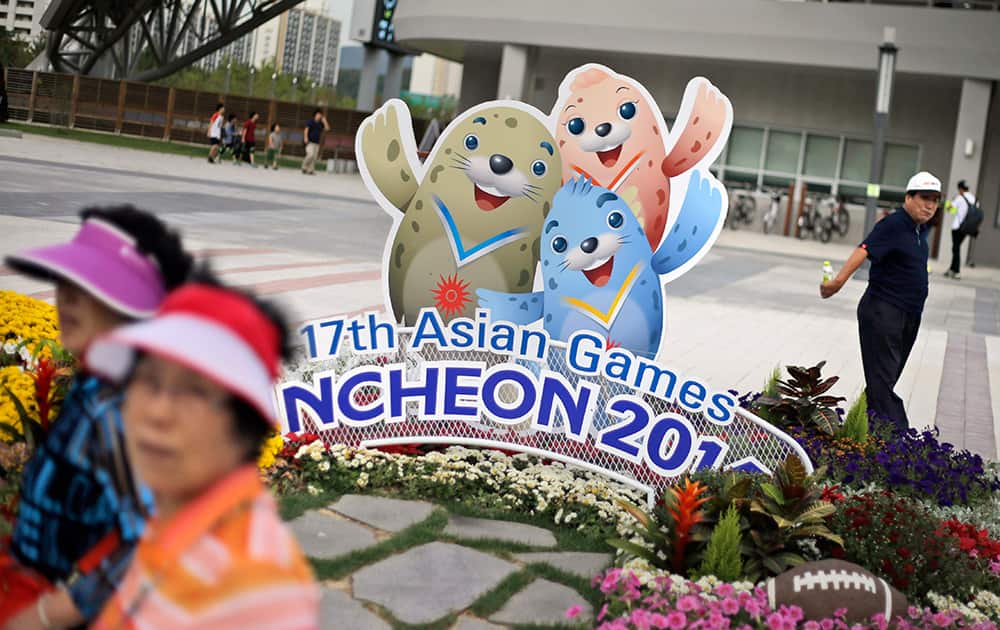 People walk past the cardboard cutouts of Barame, Vichuon and Chumuro, the mascots of the 17th Asian Games, outside a stadium in Incheon, South Korea.