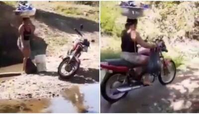 Ultimate balancing: Women drives bike across river with loaded tub on head and bucket, bag in hands